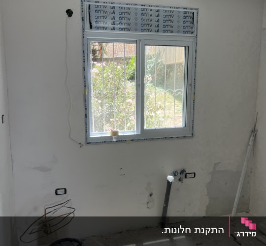 התקנת חלון אלומיניום לבן עם ארגז תריס בחדר בשיפוץ
